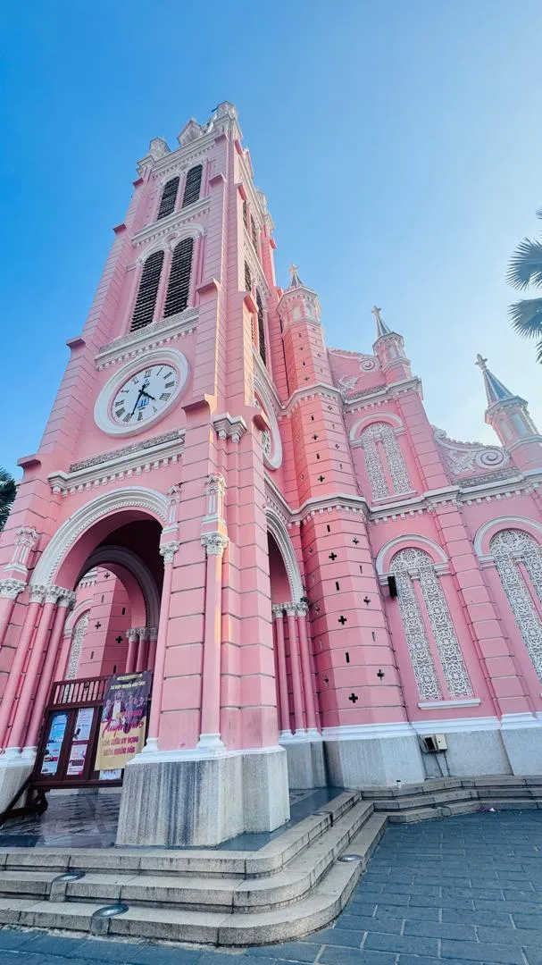 Pink church facade and clock tower beneath a blue sky in Ho Chi Minh City